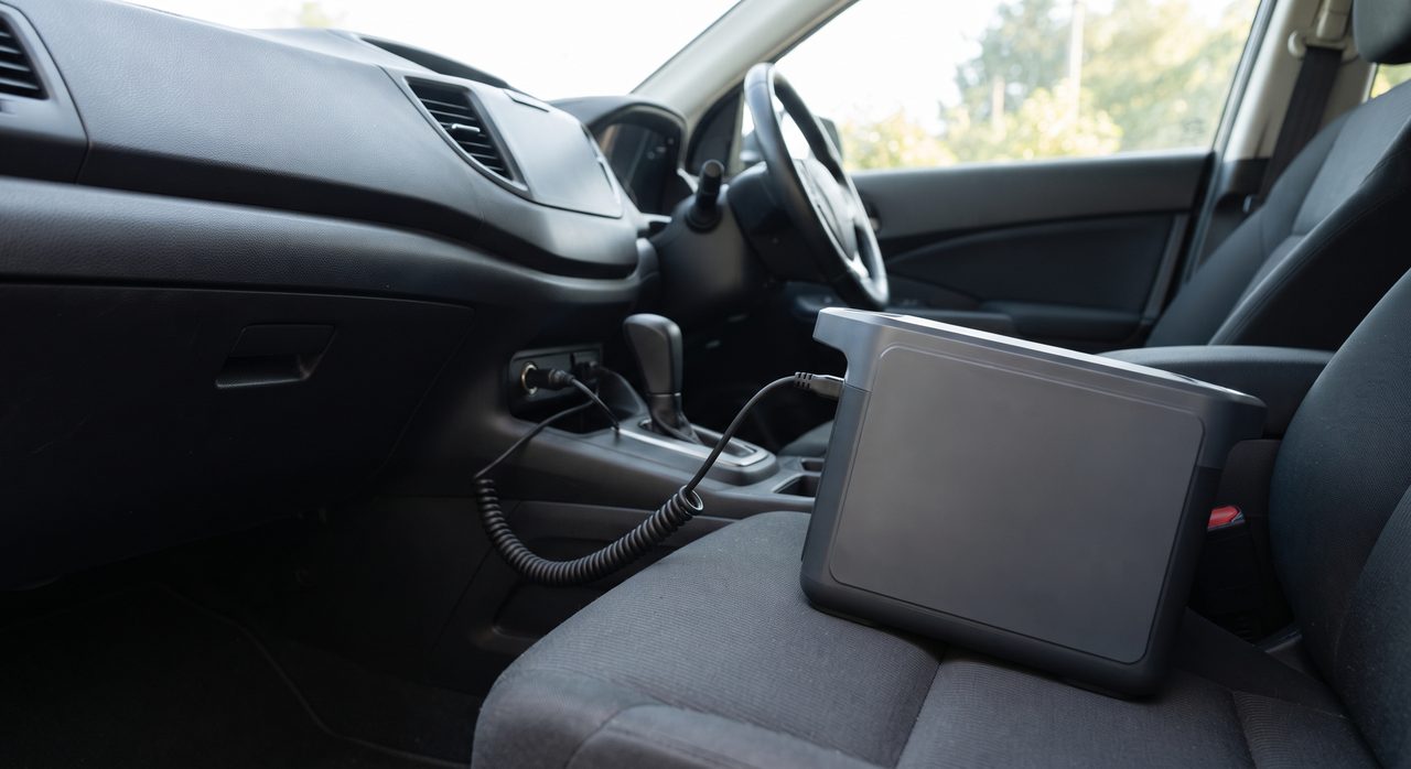 車内のシガーソケットから伸びたケーブルが座席上のポータブル電源につながる様子