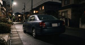 夜間の住宅街の路上に一台だけ車が停まっている、少し緊張感のある静かな情景