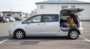 昼間の駐車場でリアゲートを開けたファミリー向けミニバン、荷室にぬいぐるみやボールが積まれている様子