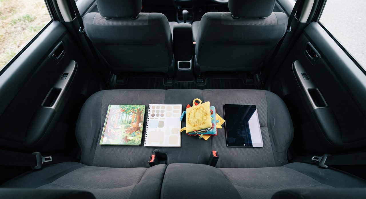 車内シートに絵本、シールブック、音の出ない布製おもちゃ、画面が暗いタブレットが並べて置かれている様子