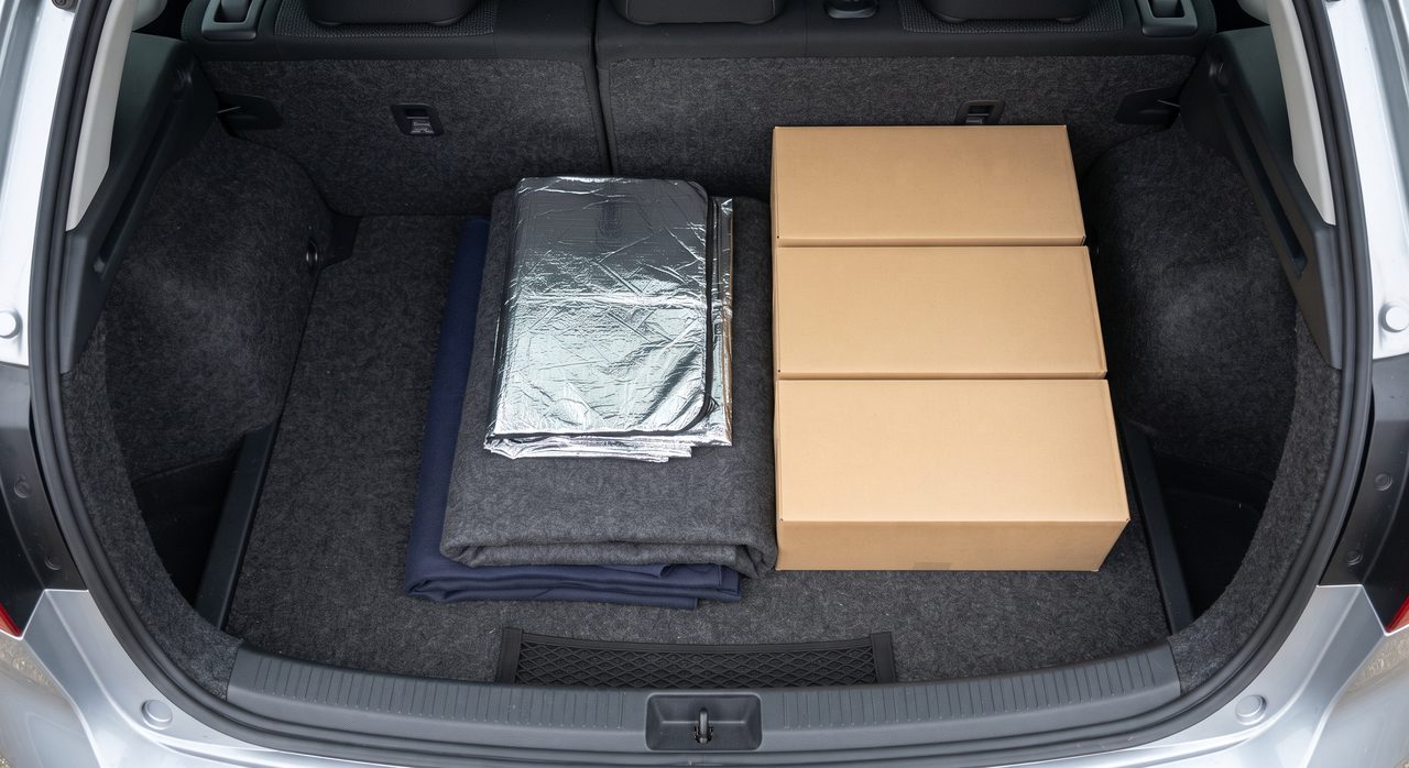 車の荷室に備蓄用の無地の段ボール箱と、銀色の保温シート・毛布などの季節対策グッズがまとめて積まれている様子