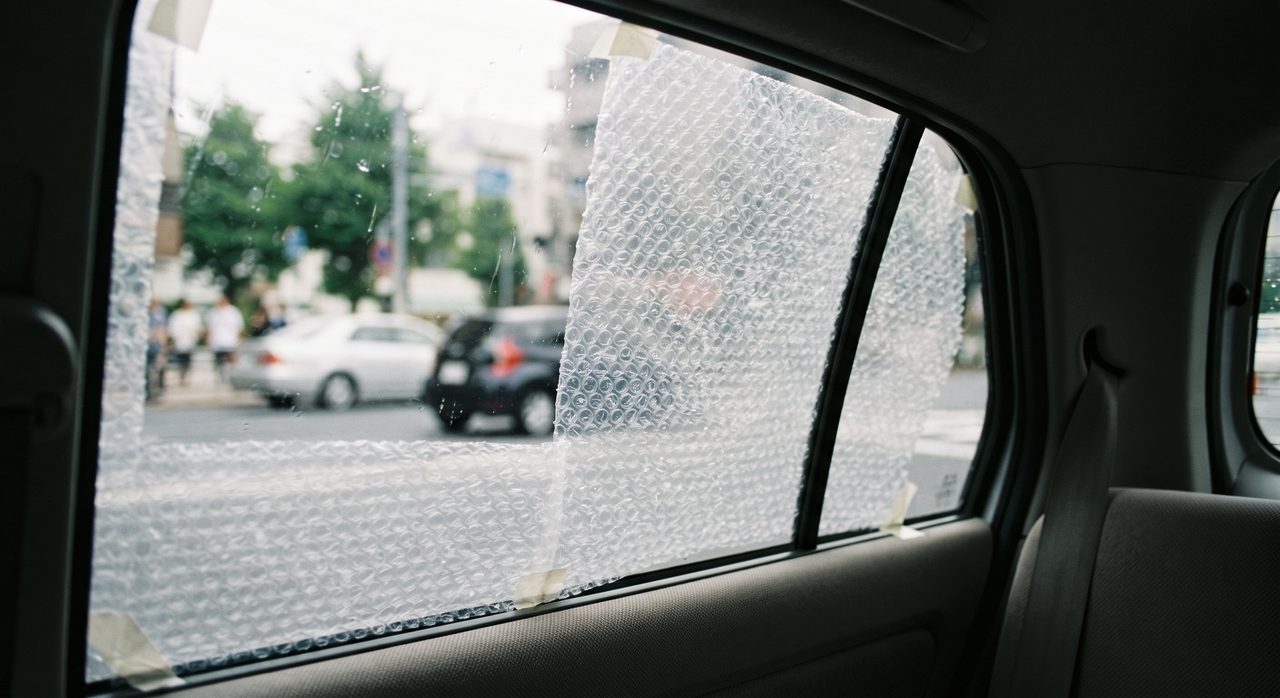 車内側から見た後部座席の窓ガラスに気泡緩衝材(プチプチ)が貼り付けられ、外の景色がぼんやりとにじんで見える様子