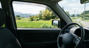 停車中の車内から見た窓が半分ほど開き、外の光と緑の景色が見える様子