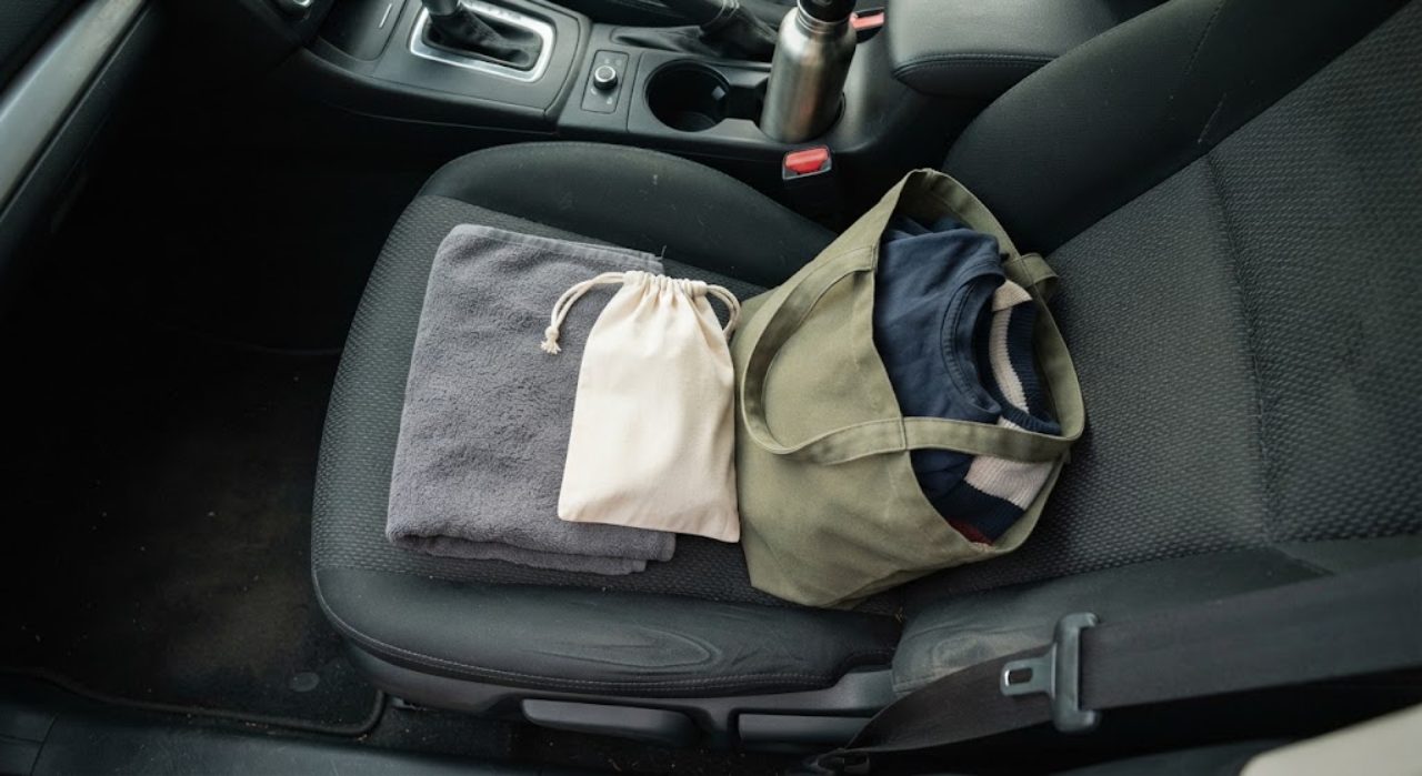 車の座席の上に無地のタオル、洗面用具ポーチ、着替えの入ったトートバッグが置かれている様子